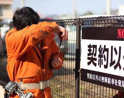 屋外フェンスに看板を取り付ける株式会社看板市場の施工スタッフ